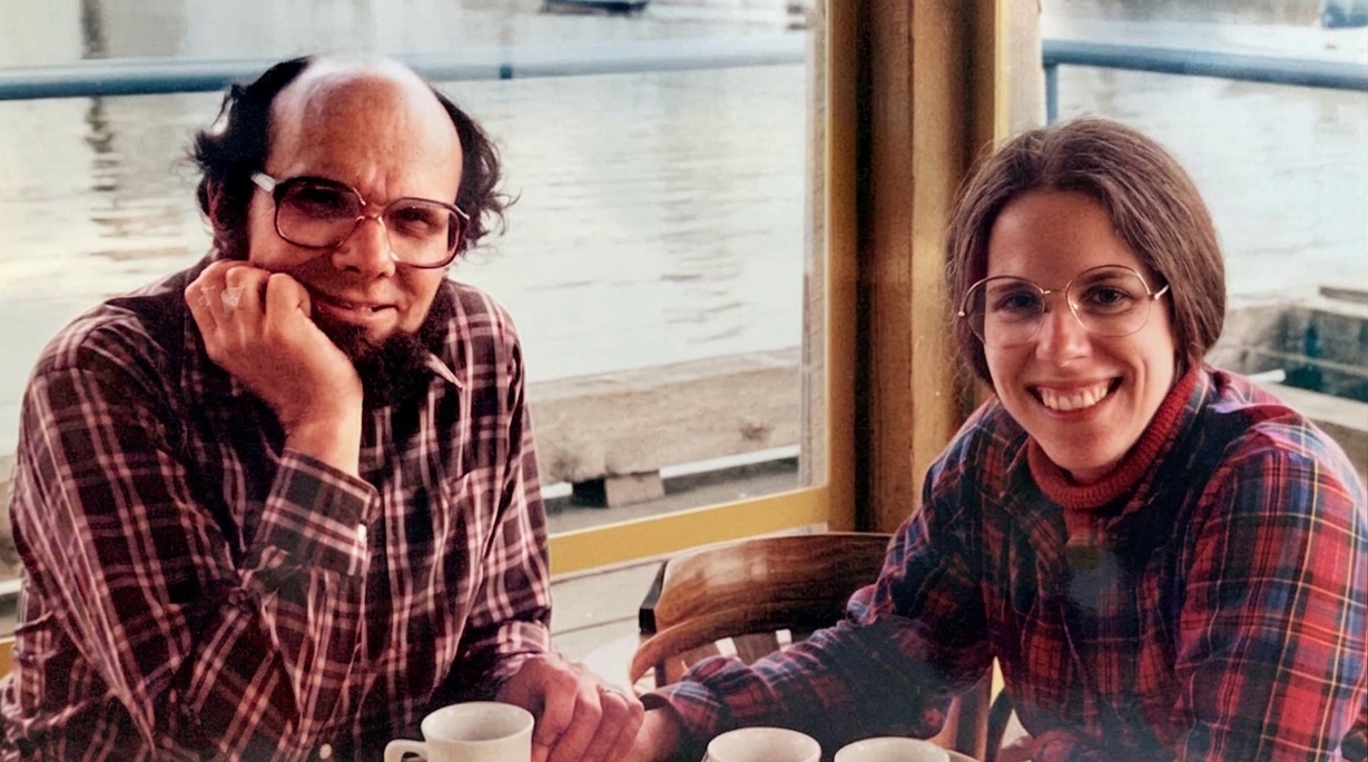 Loren and Mary Ruth Wilkinson hold hands while sitting at a table in a seaside restaurant.