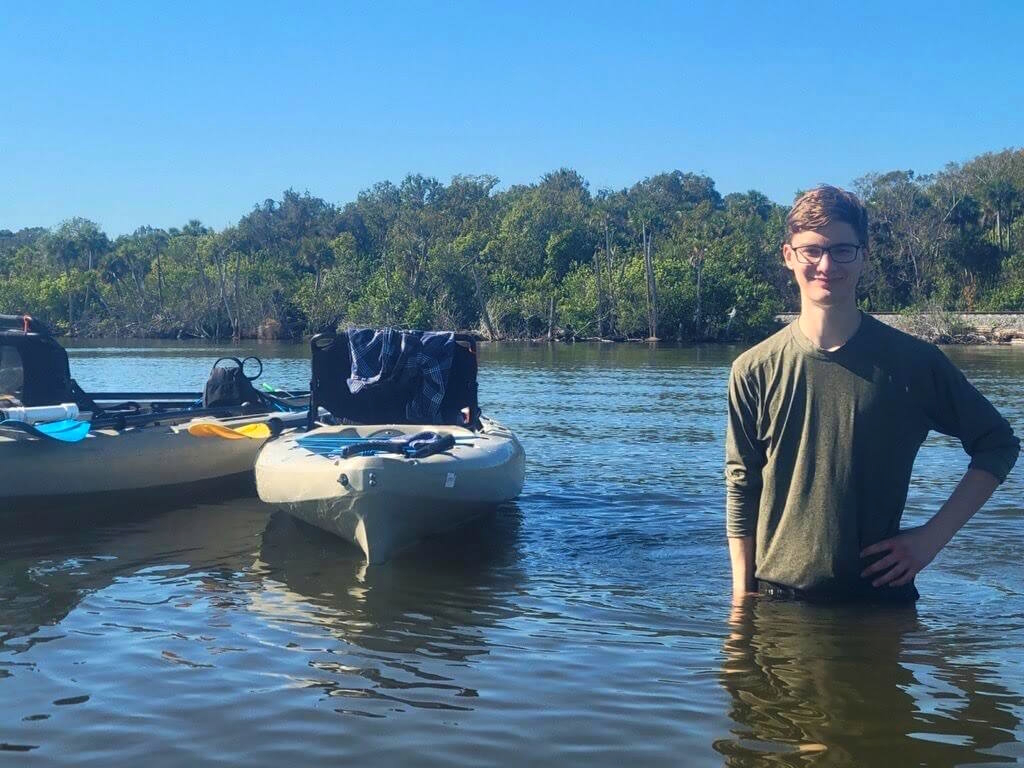 Author Noah Guthrie stands in waist-deep water next to boats carrying equipment.