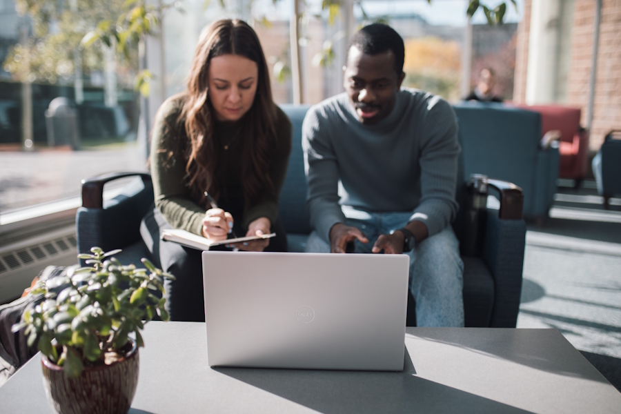 Two students sit looking at a laptop in Regent College's atrium
